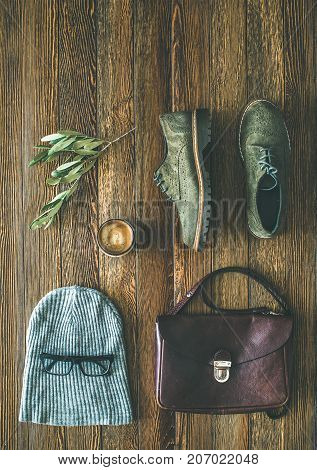Flat-lay of woman's fall accessories and coffee. Haki suede leather oxford boots, brown shoulder bag, grey cap and cup of espresso over wooden background, top view, copy space