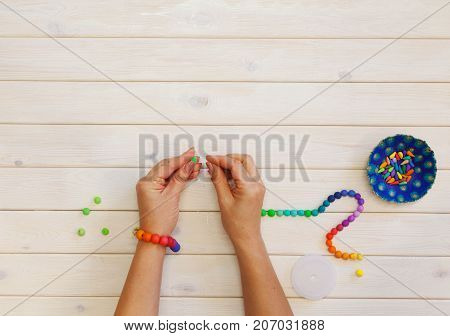 Woman making colored beads. Polymer clay. Background of white wood.