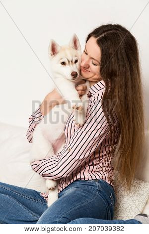 Happy beautiful woman hugging puppy husky. girl sitting on a sofa with a dog.