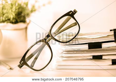 Close up black reading eyeglasses on stacking of office paper business working document and information data concept. retro color tone