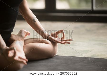 Mudra hand position close up, symbolic ritual gesture, young woman performing yoga and meditation at home, sitting in Padmasana exercise, Lotus pose, working out wearing black outfit, floor background