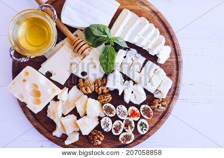 Cheese platter: Parmesan cheddar gouda gorgonzola brie and other with walnuts and honey on wooden board on white background. Tasty appetizers with different kind of cheese. Top view.