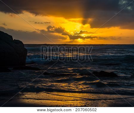 The setting sun sends out rays from behind the clouds at Noordhoek Beach