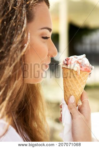 Young cheerful girl is eating ice cream on walk, on promanade.