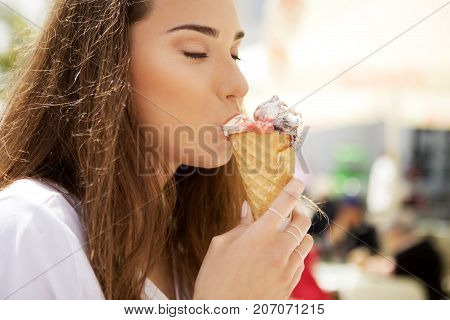 Young cheerful girl is eating ice cream on walk, on promanade.