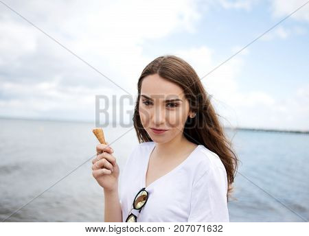 Young cheerful girl is eating ice cream on walk, on promanade.
