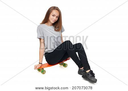 Teen girl in full length sitting on skate board smiling at camera, isolated on white background