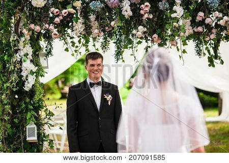 Look from behind at groom that admires and waits for a charming bride. She is walking down the aisle