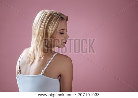 Better pose. Kind woman bowing her head while looking downwards and sitting in isolated on pink background
