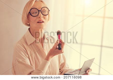 Preserve your beauty. Waist up of a nice beautiful aged woman holding a powder brush and applying dry concealer while doing her make up