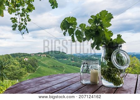 Jars with grapes and candle on wooden barrel near vineyard on south Styrian wine route in Austria