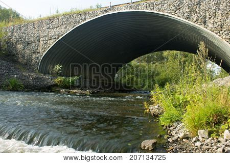 Stone car bridge across a small river in the forest.