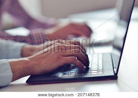 Man's hands typing on laptop keyboard in office