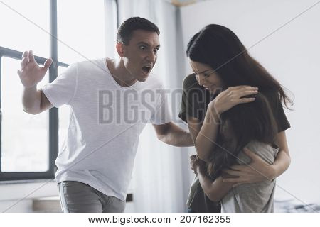 Wife And Daughter Are Embracing, While Her Husband Angrily Screams At Them And Swings To Strike