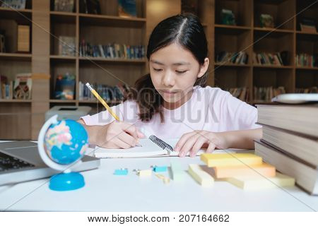Girl Reading And Writing In Library Of School.