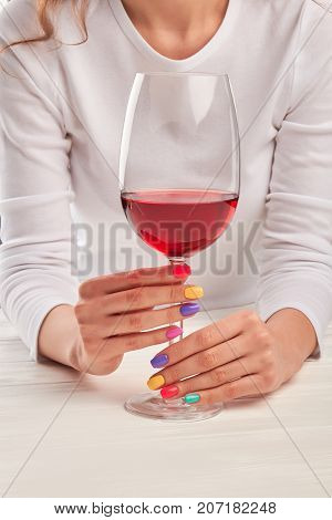 Glass of wine in manicured hands. Young woman with beautiful summer manicure holding glass of red wine. Feminine beauty and elegance.