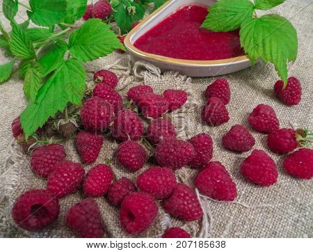 scattered on the table ripe fresh berries of raspberries along with jam.
