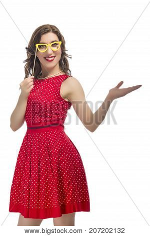 Portrait of Alluring Caucasian Female Holding Yellow Artistic Spectacles Near Eyes. Posing In Red Polka Dot Dress Against Pure White.Holding Hand in Front. Vertical Image
