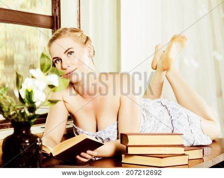 young woman reads a book lying on a desk in front of a window. old style, lolita concept.