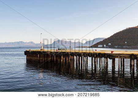 Pier lined with tires as fenders for the boats docking on them, mountains and ocean in the background, the city of Harstad in Norway