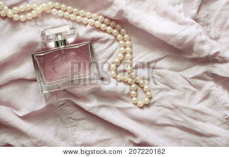 Women's perfume and pearl beads on a pink delicate fabric. Toning.