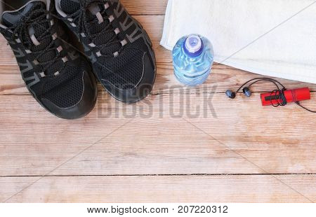 Sport equipment shoes water earphone and towel on wooden background