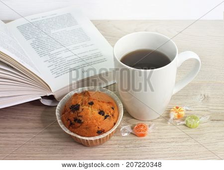 Leisure. A cup of coffee a cupcake and a book on the table.