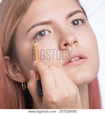 Beautiful young girl applying make up on eyes. Isolated on grey