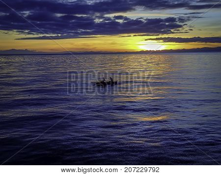 two fishermen on small fishing boat in the middle of the blue sea at sunrise