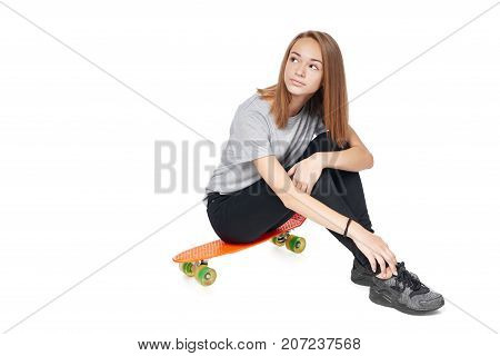 Teen girl in full length sitting on skate board looking away at blank copy space, isolated on white background