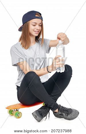 Teen girl in full length sitting on skate board opening a bottle with water, isolated on white background