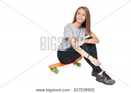 Teen girl in full length sitting on skate board looking away at blank copy space, isolated on white background