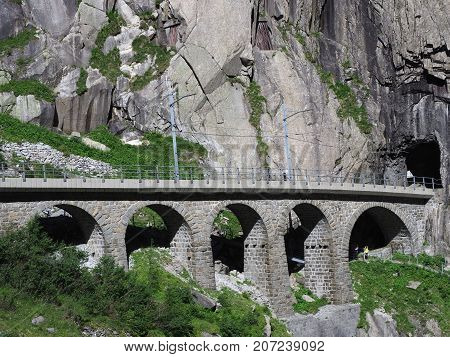 Scenic stony rail bridge in swiss Alps in SWITZERLAND near Andermatt town with alpine rocky mountains landscape scenery in 2017 warm summer day, Europe on July.