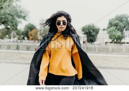 Portrait Of Stylish Modern Young Curly Woman In Coat Sunglasses. She On The Street And Looks Happy.