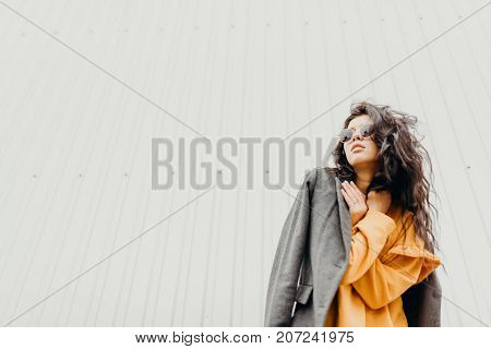 Portrait Of Stylish Modern Young Curly Woman In Coat Sunglasses. She On The Street And Looks Happy.