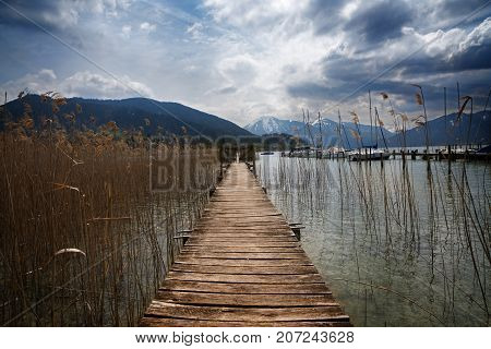 Wooden jetty with a gate in the tegernsee lake snow-covered mountains and a clowdy sky in the background landscape in the famous tourist resort in the bavarian alps bavaria germany europe