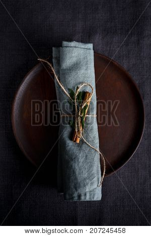 Top view of wooden plate with plain napkin wrapped and decorated with cinnamon stick.