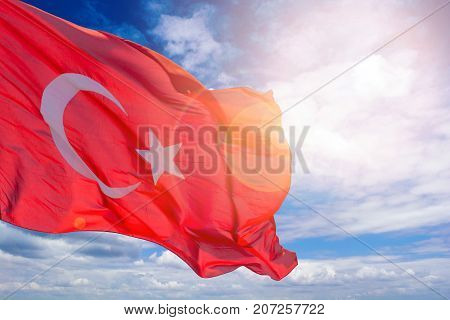 Turkish flag against a blue cloudy sky. Flag of Turkey in sunlight and glare. Red flag with a crescent and a star.