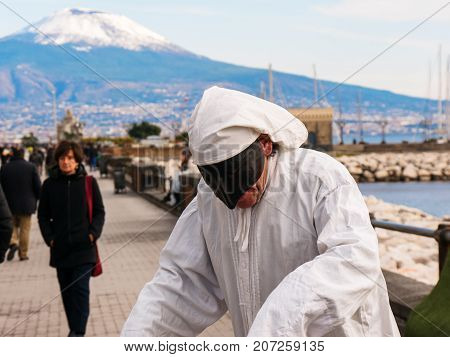 Naples 2017 January Italy: Pulcinella and people, traditional Neapolitan mask gestures with snowy Vesuvius in the background in the Gulf of Naples. Actor recites the part of Pulcinella in the street, among the people who pass, on the promenade of Naples