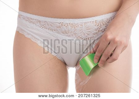 A girl in white and pink panties shaves her hair in the bikini area with a razor and makes depilation with cream