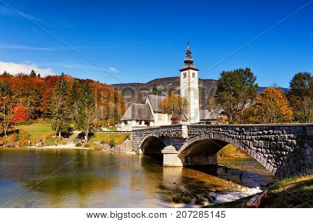 Colorful Autumn Day In Ancient Village With Old Bridge And Church