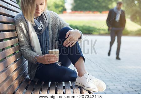 Lonely sad woman is sitting on the bench and holding coffee