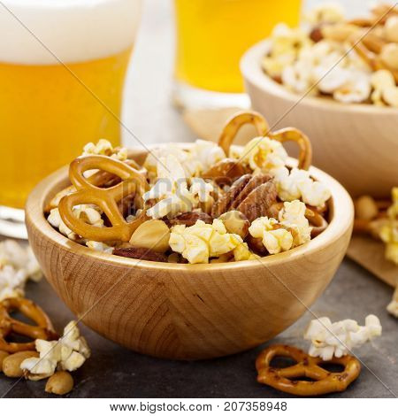 Homemade trail or snack mix with popcorn, pretzels and nuts with beer in glasses