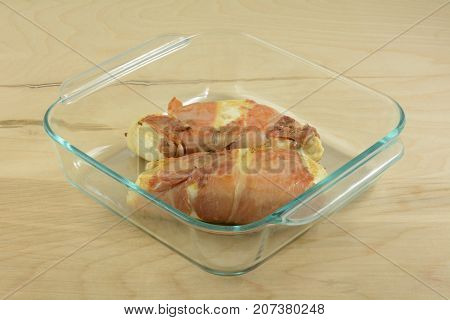 Seared prosciutto wrapped chicken breasts in glass baking pan in preparation for baking