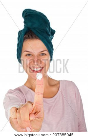 Smiling young woman with bathtowel on head and moisturizing cream on her finger on isolated