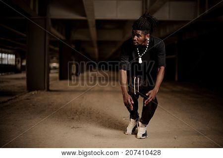 Young afro american man with dreadlocks and dressed in black clothes in the half squat. Full length