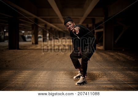Emotional full length portrait of afro american man in the half squat dressed in trendy black clothes