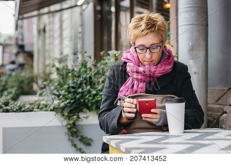 Adult pretty woman browsing smartphone in outside cafe.
