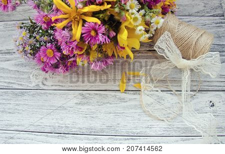 Bouquet of bright purple and yellow autumn flowers a spool of thread and a bow made of a lace ribbon on a gray wooden background (with copy space for your text selective focus) as a rustic background retro style
