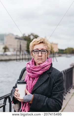 Portrait of adult woman with takeaway coffee cup standing on esplanade.